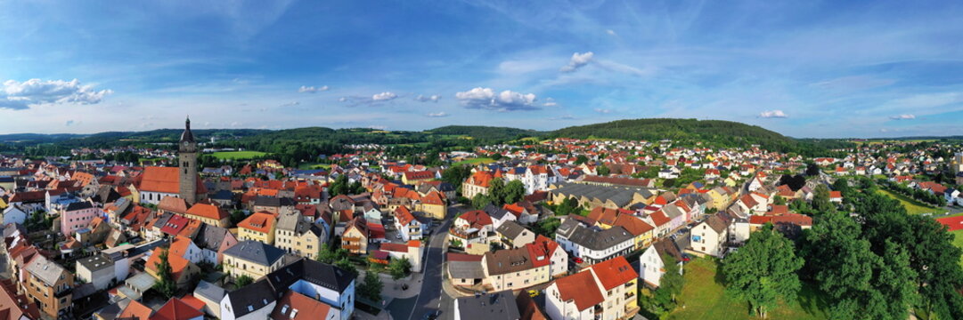 Malerische Luftaufnahme von Auerbach in der Oberpfalz mit der markanten Stadtpfarrkirche, traditionellen roten D&auml;chern und idyllisch gr&uuml;ner Landschaft im Hintergrund unter blauem Himmel.