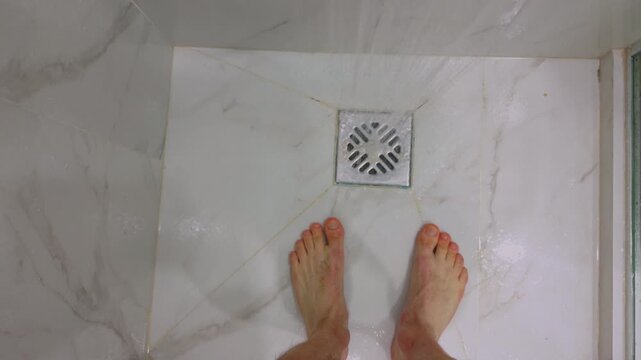 First-person POV of a man walking into a shower, turning on water. Everyday routine, personal hygiene, home lifestyle, morning self-care. Person enters bathroom, flows. Male feet are standing, drain.