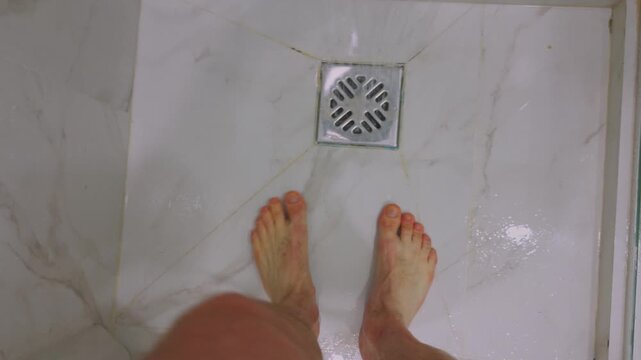 First-person POV of a man walking into a shower, turning on water. Everyday routine, personal hygiene, home lifestyle, morning self-care. Person enters bathroom, flows. Male feet are standing, drain.