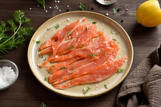 Slices of salted salmon on plate on dark wooden table