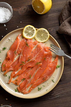 Slices of salted salmon on plate on dark wooden background