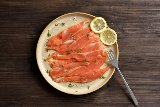 Slices of salted salmon on plate on dark wooden background