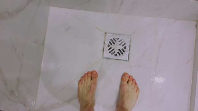 First-person POV of a man walking into a shower, turning on water. Everyday routine, personal hygiene, home lifestyle, morning self-care. Person enters bathroom, flows. Male feet are standing, drain.