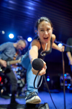Young woman singer extends microphone during blue stage sound check