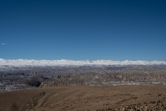 Brown plateau slopes above Zanda badlands and snowy peaks