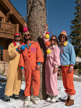 Group of Friends in Colorful Onesies Posing Outdoors near Wooden Chalet in Winter