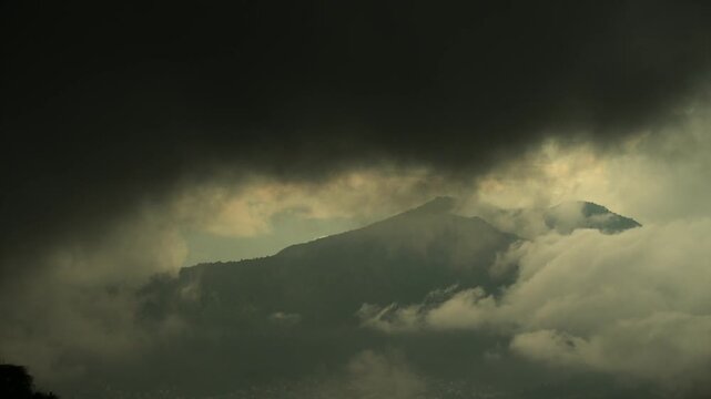 Thick clouds thicken around a mountain peak while a warm sliver of light traces the ridge in Nepal