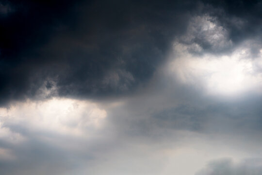 Dramatic dark clouds with hints of light creating a moody sky atmosphere. A captivating view of dark, swirling clouds illuminated by soft light, evoking a sense of drama and anticipation in the sky.