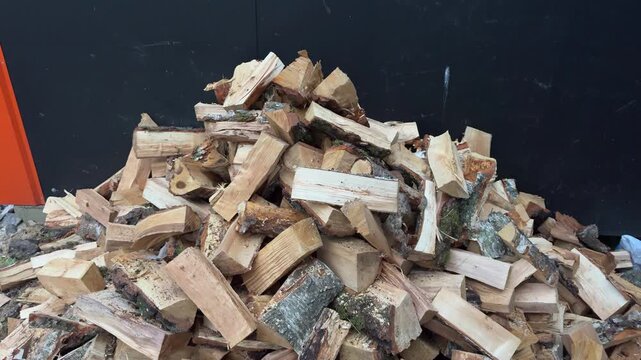 Split firewood logs stacked in a large pile against a dark wall, wood storage, home heating, natural fuel, winter preparation
