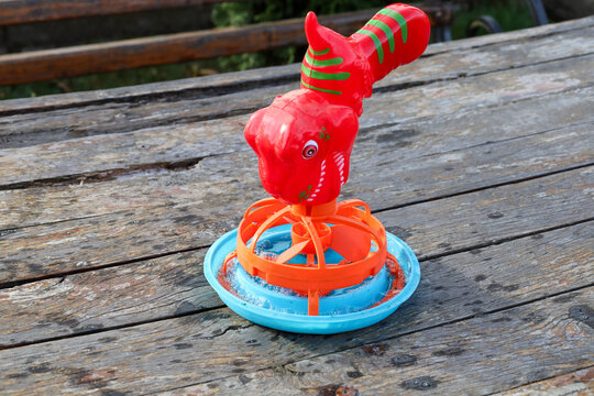 A bright children's bubble toy in the shape of a dinosaur stands in a blue saucer on a wooden table. The plastic bubble maker is prepared for a fun outdoor game in the garden. Colorful entertainment b
