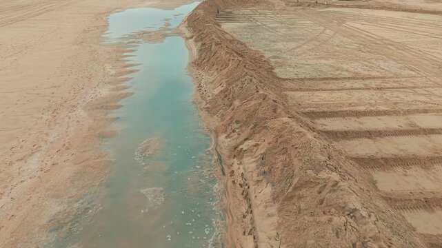Aerial drone view of tall protective sand berms beside a shallow water channel at Newport Beach, designed to prevent coastal flooding.