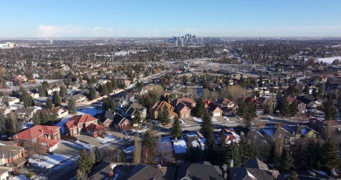 Aerial flyover of a snow-covered residential neighborhood with downtown Calgary in the distance, Alberta, Canada.