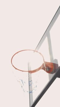 Vertical low angle shot of an athletic young man jumping to reach a basketball hoop against a bright cinematic sun flare sky, goal concept