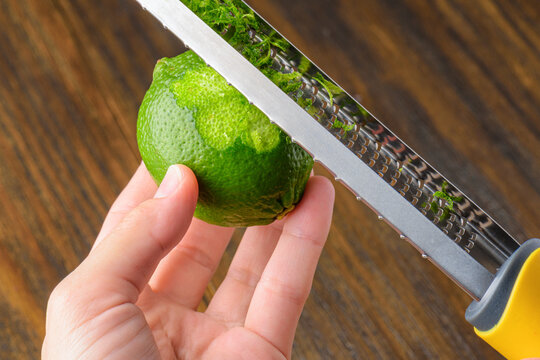 Female hands grating bright green lime on sharp zester tool