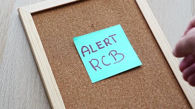 Cyan sticky note reading ALERT RCB, the Polish government emergency alert system, pinned on a framed cork board. Suits emergency warnings, crisis management, civil protection, public safety and weath