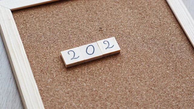 With 2027 finally complete on the cork board, a hand pulls back from the last tile, leaving a neat row of handwritten numbers. Fits annual planning, business year kickoff, project calendars and the y