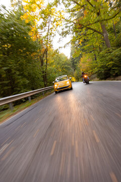 Motorcyclist Overtaking a Small Yellow Car on a Forest Road