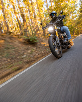 A motorcyclist overtakes a small yellow car on an asphalt road through the forest. The moving shot captures both vehicles in motion against a wooded roadside backdrop.