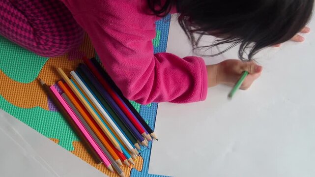 家のリビングでカラフルな色鉛筆で絵を描いている幼児の子供の姿