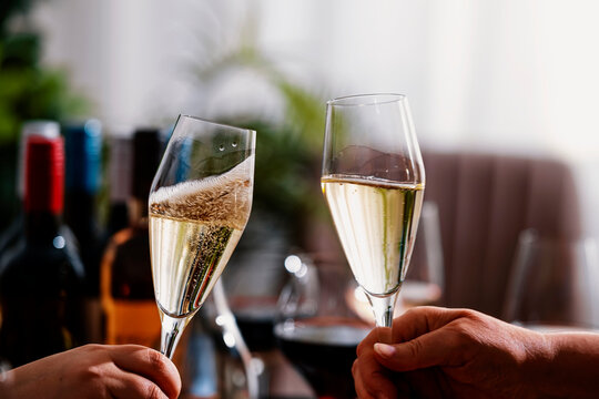 Close up of hands clinking cava wine flutes at lunch table, autumn festive celebration concept. Luxury hospitality gathering. Toasting sparkling champagne during cozy family dinner setup.