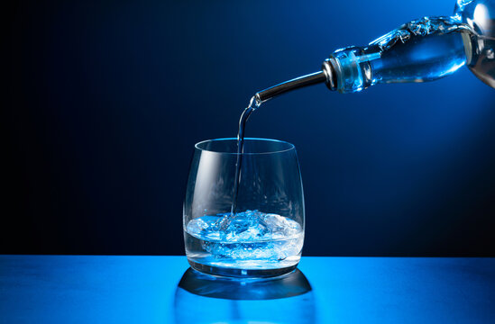 Vodka pours from bottle to glass with ice.