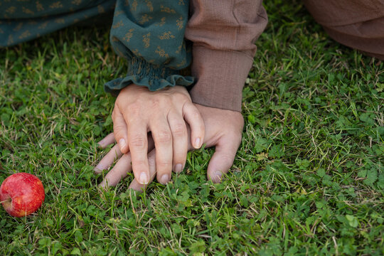 Hands of two people touching on green grass with an apple nearby  