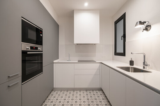 Modern kitchen with sleek white cabinets, gray accents, and patterned floor tiles. Features built-in appliances and a minimalist design.