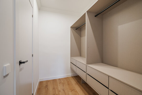 A modern, minimalist closet interior with light wood flooring. The space features built-in shelves and drawers, creating a clean and organized look.