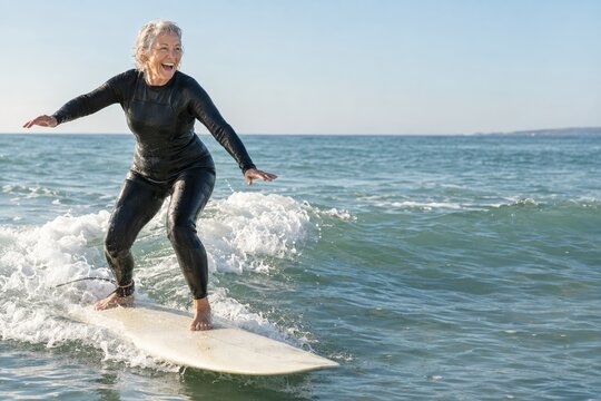 Senior woman standing up on a surfboard for the first time on a small white wave, learning to surf at 71 with copy space