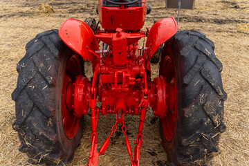 Close view of the rear hitch, axle, differential housing and large treaded tires of a red farm tractor parked on dry stubble. © Marina