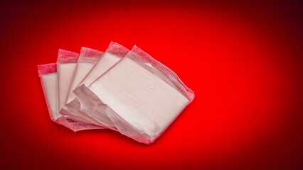 Stack of individually wrapped sanitary pads on a vibrant red background © İdil Toffolo