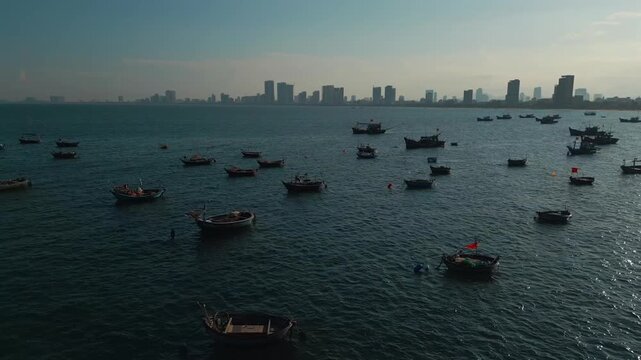 fishing boats anchored in sea bay with Danang city skyline on horizon, high angle coastal seascape view in Vietnam, aerial drone view