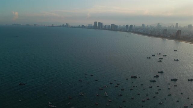 fishing boats anchored in sea bay with Danang city skyline on horizon, high angle coastal seascape view in Vietnam, aerial drone view