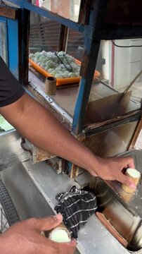 A street vendor making kue putu (green coloured rice cake) in a traditional wooden cart, selling around housing complex