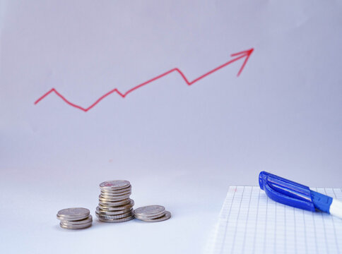 Stacks of coins with an upward trending graph drawn on white paper, representing financial growth, savings, investment and business success.