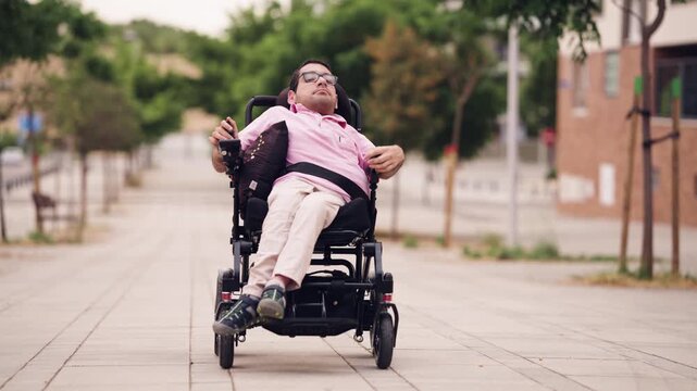 Man with a physical disability, spina bifida, moving along a sidewalk in his modern motorized wheelchair. Empowering independent living