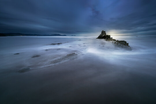 Rocky flysch formation on beach shore during blue hour with silky long exposure sea water, Sopelana beach in Bizkaia, Cantabrian sea, Spain