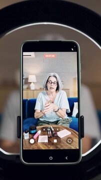 Smartphone screen showing a senior influencer vlogging. Elegant woman live streaming a makeup tutorial for her social media channel. Vertical
