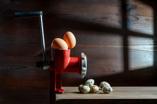 Vintage red meat grinder transformation concept with chicken and quail eggs. Conceptual still life with old manual mincer and fresh eggs. Chicken eggs inside grinder changing into small quail eggs