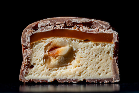 Chocolate bar cross section with caramel nougat and nut. Macro cut chocolate candy texture. Layers of milk chocolate rich caramel soft nougat and whole peanut inside sweet dessert for bakery menu