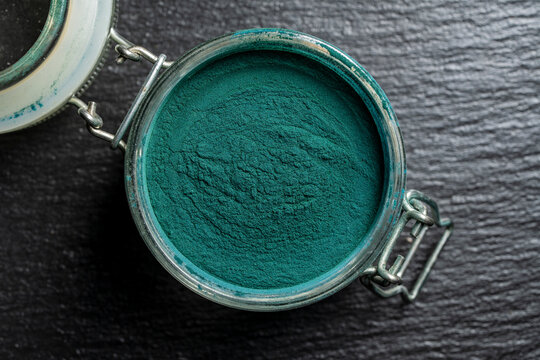 Spirulina powder in glass jar on dark background. Top view of organic green chlorella or spirulina powder inside open jar. Superfood supplement backdrop for healthy diet, wellness, detox and marketing