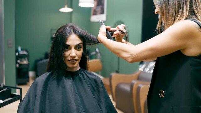 Professional hairstylist trimming a female client's hair in a modern beauty salon. Brunette woman getting a haircut and new hairstyle