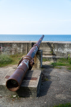 Old rusty artillery cannon on concrete fortification overlooking the blue ocean sea horizon view
