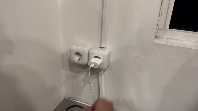 people plugging smartphone charger to electric wall socket
