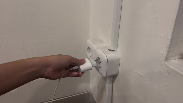 people plugging smartphone charger to electric wall socket