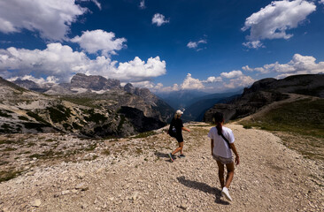 Fototapeta premium People hiking a mountain trail with backpack in summer Dolomites Italy