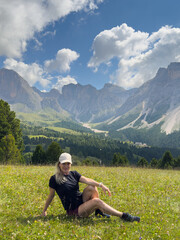 Fototapeta premium Young woman lies relaxed on grass in a mountain meadow wearing casual clothes enjoying nature and tranquility on a sunny day. 