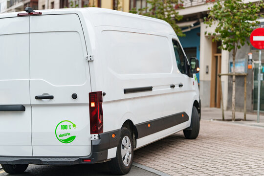 A white electric commercial cargo van parked on a city street during delivery service.