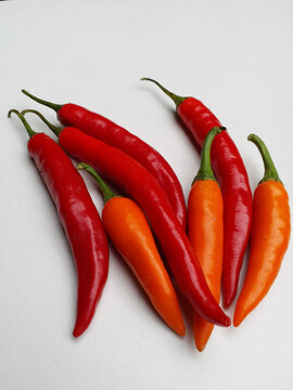 Vertical top view of fresh raw red and orange chili peppers group isolated on minimal white background. Perfect for spicy food menus, cooking posters, culinary packaging, or print sticker.