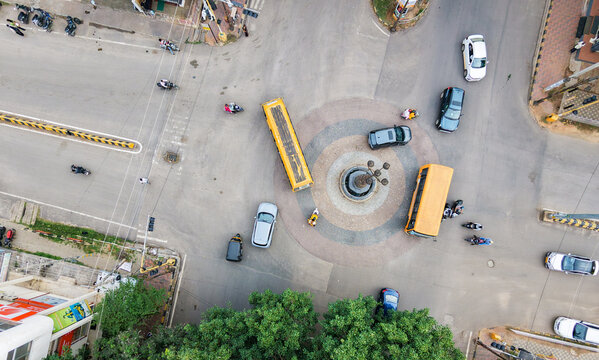  Drone shot of a busy traffic circle, aerial view shows cars, school buses navigating the bustling urban roundabout during Dussehra festival in Mysuru, India.